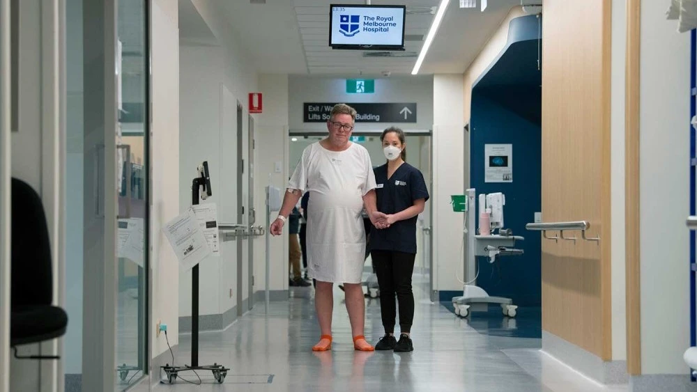 Male patient guided down corridor by physiotherapist