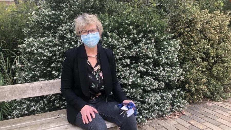Professor Jo Douglass sits on bench in front of flowering bush