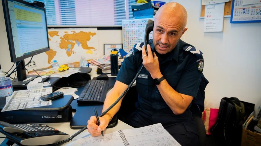 Male police officer on office phone taking notes (Image copyright Victoria Police)