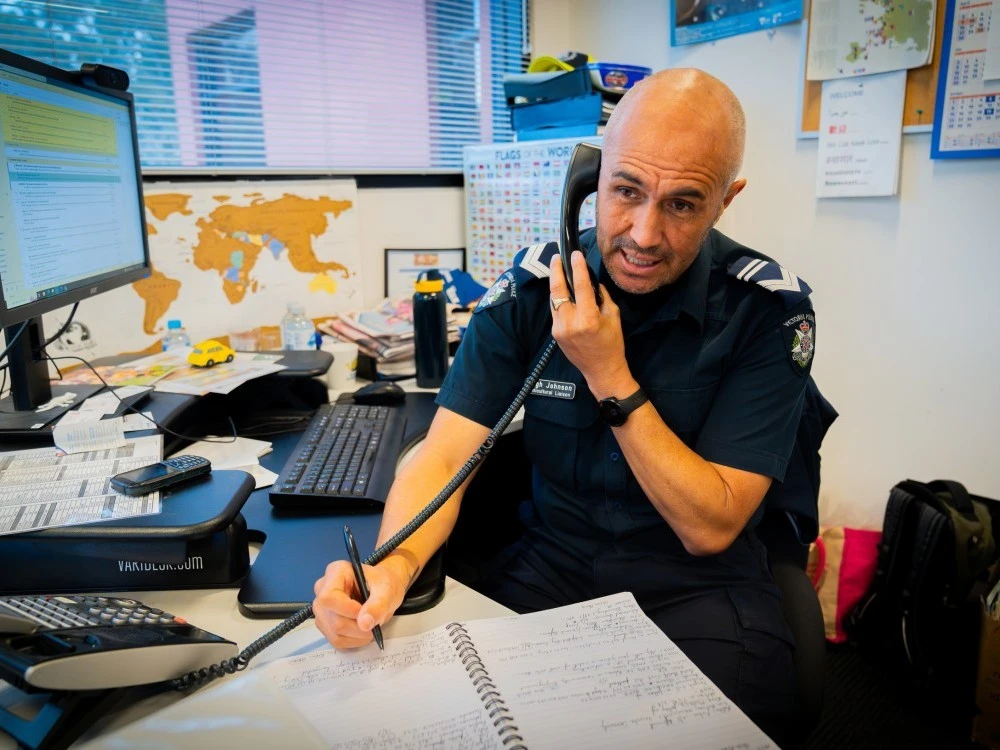 Male police officer on office phone taking notes (Image copyright Victoria Police)