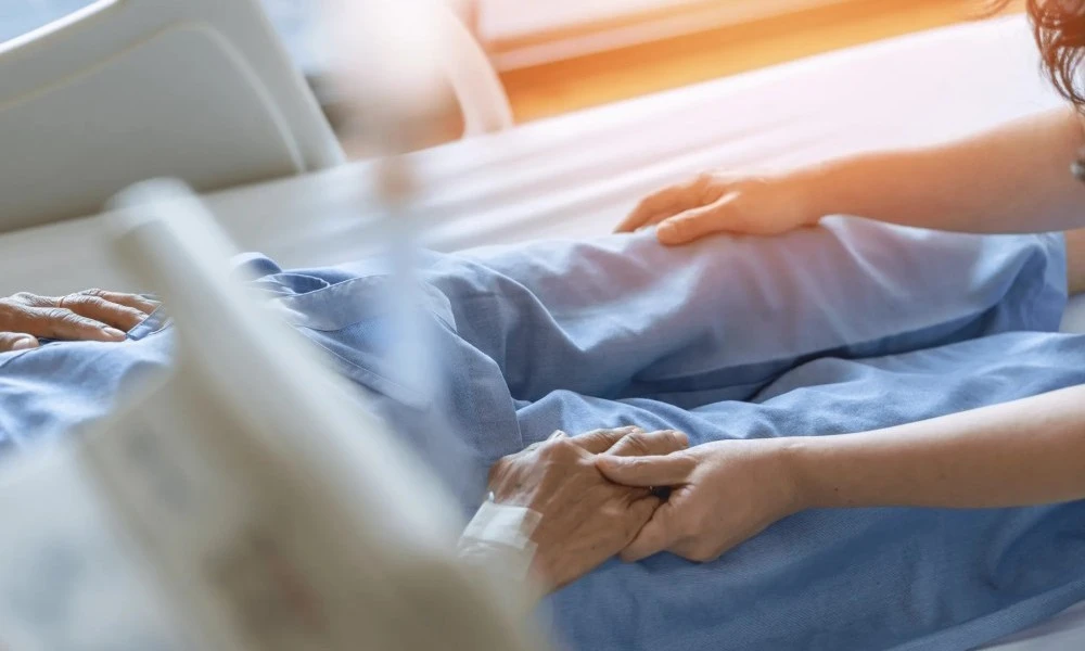 Patient in bed holding another person's hand