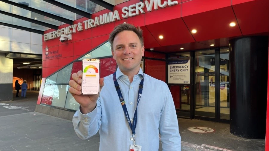 Ben outside ED entrance with emergency wait times dashboard displayed on his phone