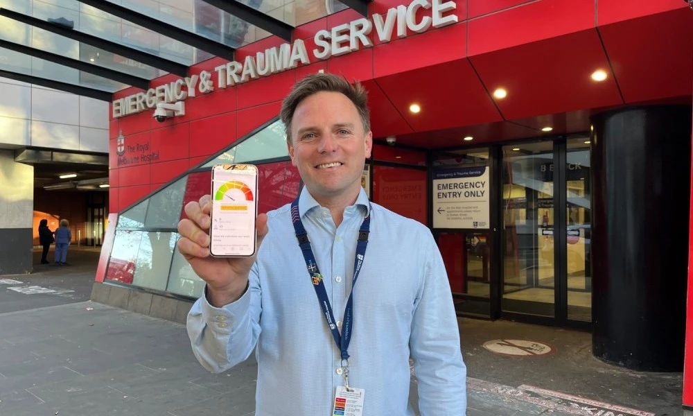 Ben outside ED entrance with emergency wait times dashboard displayed on his phone