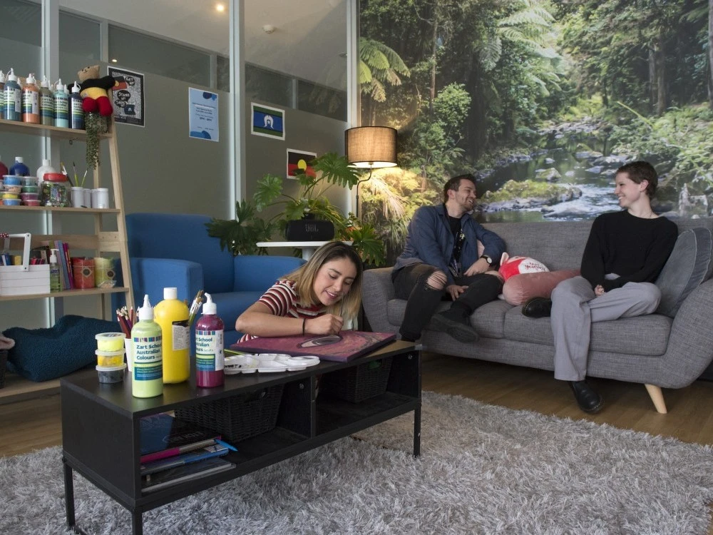 Visitor paints while another talks to a peer worker on a couch at Safe Haven