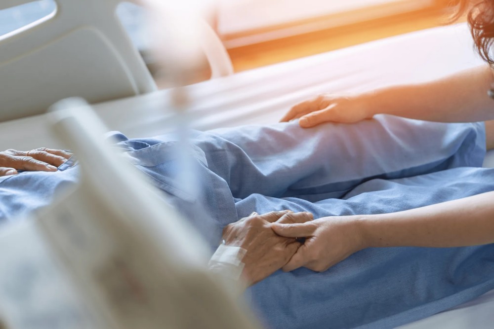 Patient in bed holding another person's hand